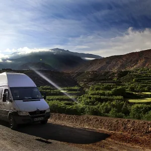 A van on a road with breathtaking views of the green fields of the mountains
