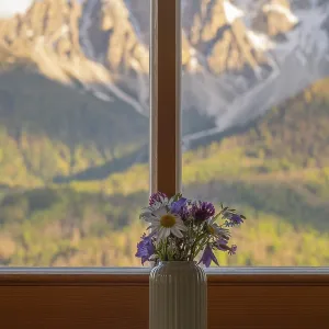 A vase with meadow flowers stands on the windowsill in the background the mountains of the Dolomites A vase with meadow flowers stands on the windowsill in the background the mountains of the Dolomites