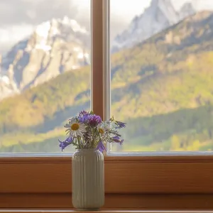 A vase with meadow flowers stands on the windowsill in the background the mountains of the Dolomites A vase with meadow flowers stands on the windowsill in the background the mountains of the Dolomites