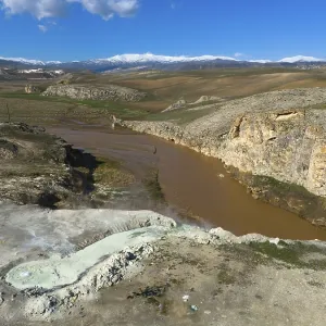 Vast landscape with brown river and rocky gorge under blue sky and white clouds