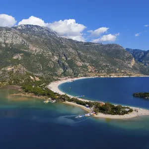 View of a beach with a peninsula surrounded by mountains and blue sea under a clear sky with clouds