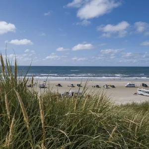 View over dunes to a car beach on the North Sea with campervans by the sea under a blue sky View over dunes to a car beach on the North Sea with campervans by the sea under a blue sky