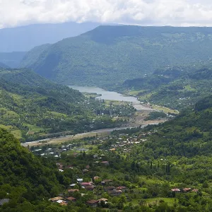 View of a green valley with a river surrounded by mountains and small villages under cloudy sky