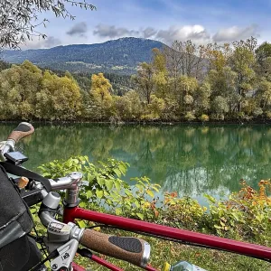 View over the handlebar of a shimmering green river in front of autumn trees and mountains