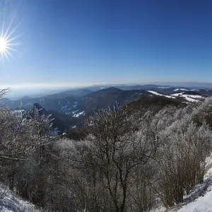 View over the hills and valleys from the mountain with hoarfrost on the branches in winter