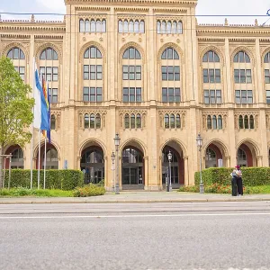 Front view of an imposing historic building with flags and green plants