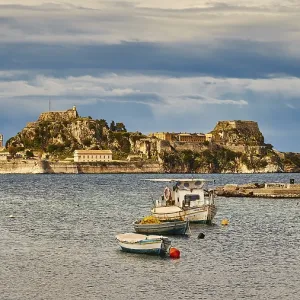 View of an island with fortress and small boats in the water under cloudy sky View of an island with fortress and small boats in the water under cloudy sky