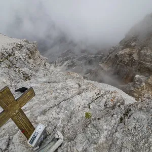 View obscured by clouds from the top of the Cima di Mezzo mountain (3154 m) with a beautiful cross on the top