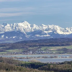 A view of a peaceful village and snow-capped Alps towering over the vast countryside A view of a peaceful village and snow-capped Alps towering over the vast countryside