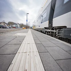 View along an empty sidewalk at a train station under a grey sky