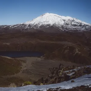 View of a snow-capped mountain and a lake in a rocky landscape under a blue sky View of a snow-capped mountain and a lake in a rocky landscape under a blue sky
