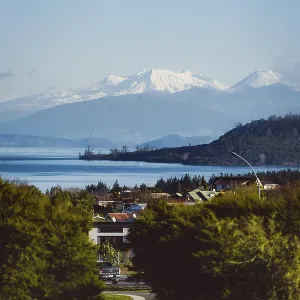 View of snow-capped mountains and a lake with a village in the foreground under a clear sky