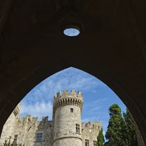 View through a stone arch to a medieval castle with tower under a blue sky