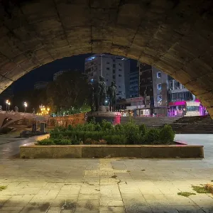 View through a stone archway of an illuminated square with monuments at night