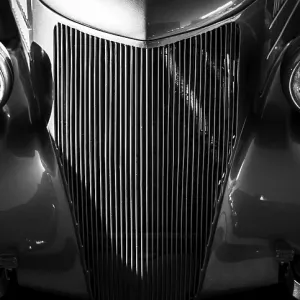 Front view of a vintage car in black and white with prominent headlights and grille in St