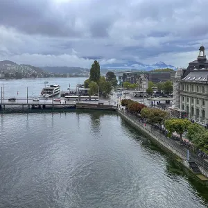 View of waterfront with boats and mountains in the background under cloudy sky