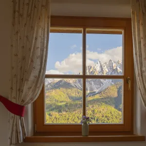 View through a window to the Dolomites in the foreground a small vase with meadow flowers on the windowsill View through a window to the Dolomites in the foreground a small vase with meadow flowers on the windowsill