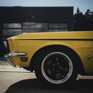 Side view of a yellow classic car in front of a modern garage in sunlight
