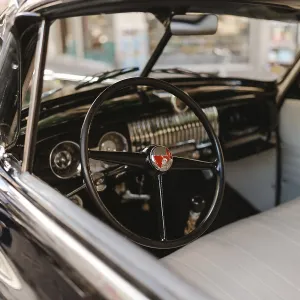 A vintage car with a black steering wheel and a white dashboard A vintage car with a black steering wheel and a white dashboard