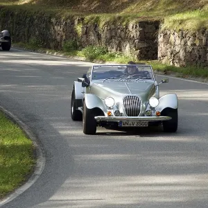 Vintage car convoy on a winding road next to a stone wall