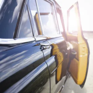 A vintage car with an open door on a sunlit road