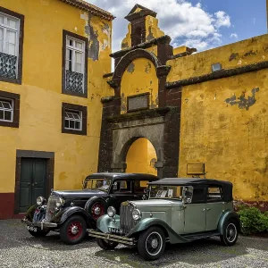 Vintage cars parked in front of yellow gate and wall