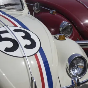 White classic car with racing stripes and number next to a red vehicle White classic car with racing stripes and number next to a red vehicle