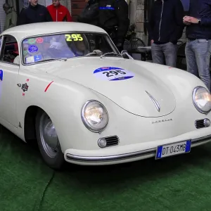White Porsche 356 with glowing headlights drives across green carpet during a vintage car rally White Porsche 356 with glowing headlights drives across green carpet during a vintage car rally