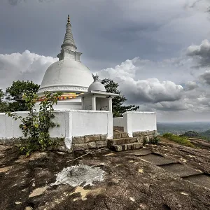 White stupa on rocky hill surrounded by cloudy skies and lush nature White stupa on rocky hill surrounded by cloudy skies and lush nature