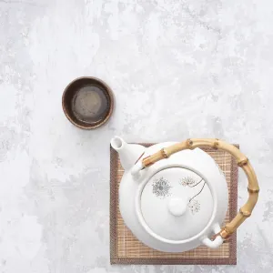 White teapot with bamboo handle and small wooden teacup on bamboo mat White teapot with bamboo handle and small wooden teacup on bamboo mat