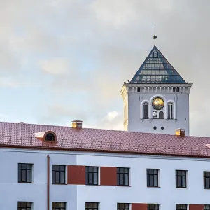 A white tower with a clock and a fragment of a modern building on the background of the sunset sky A white tower with a clock and a fragment of a modern building on the background of the sunset sky