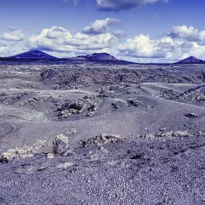 Wide, dry volcanic landscape with rolling hills and mountains under a cloudy blue sky