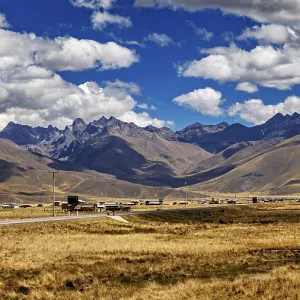 Wide landscape with a road between rolling mountains under a blue sky with clouds