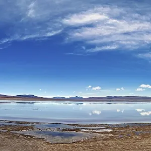 Wide and open landscape with a lake under dramatic skies and distant mountains