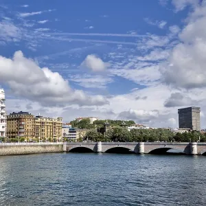 Wide view of a city bridge with river and surrounding buildings under a blue sky Wide view of a city bridge with river and surrounding buildings under a blue sky