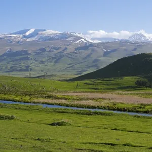 A wide view over a green valley with snow-capped mountains under a clear sky A wide view over a green valley with snow-capped mountains under a clear sky