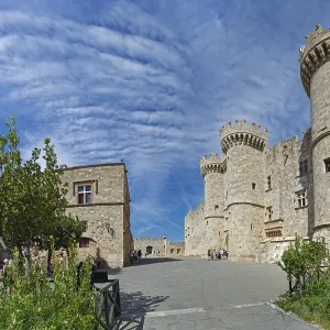 Wide view of a medieval castle with towers and stone walls under a cloudy sky