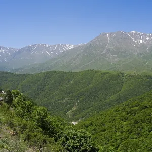 A winding mountain road snakes through green hills with mountains in the background