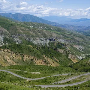 A winding road winds through the green mountains under a blue sky A winding road winds through the green mountains under a blue sky