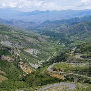 Winding roads lead down through a green valley into mountainous terrain under a clear sky Winding roads lead down through a green valley into mountainous terrain under a clear sky