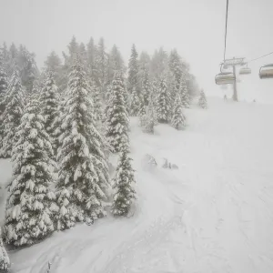 Winter forest and chairlift in snowfall at alpine ski resort