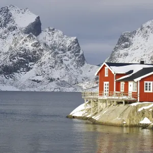 Wintery, Nordic landscape with red holiday home standing directly by the fjord