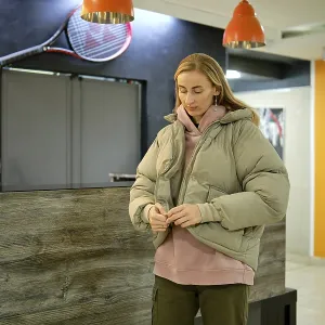 A woman is adjusting her puffer jacket while standing at the reception area of a sports center