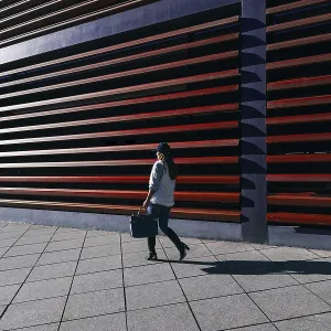 Une femme vêtue de manière informelle passe devant un bâtiment moderne avec des lattes horizontales distinctives. Une femme vêtue de manière informelle passe devant un bâtiment moderne avec des lattes horizontales distinctives.