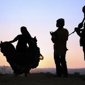 Woman dancing in front of the setting sun with two musicians Woman dancing in front of the setting sun with two musicians