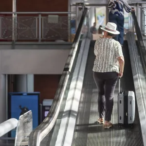 Woman in a hat pulling luggage up an escalator