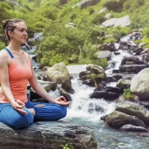 Woman in Hatha yoga asana Padmasana outdoors at tropical waterfall Woman in Hatha yoga asana Padmasana outdoors at tropical waterfall
