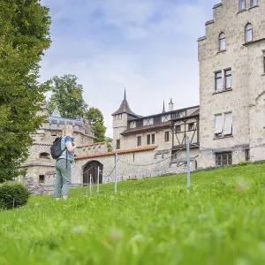 A woman next to a historic building with a green meadow and trees in the background