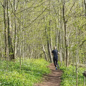 Woman running on a nature trail in a lush forest with budding leaves on the trees