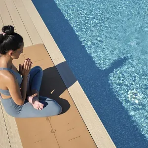 Eine Frau sitzt gekreuzt auf einem Yoga-Mat am Pool. Eine Frau sitzt gekreuzt auf einem Yoga-Mat am Pool.